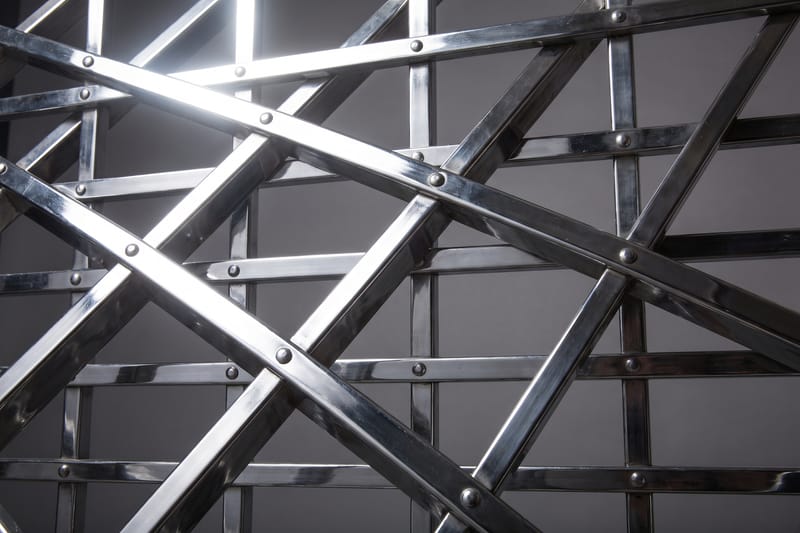 A wrought-iron portcullis lattice raked by a single hard light.
